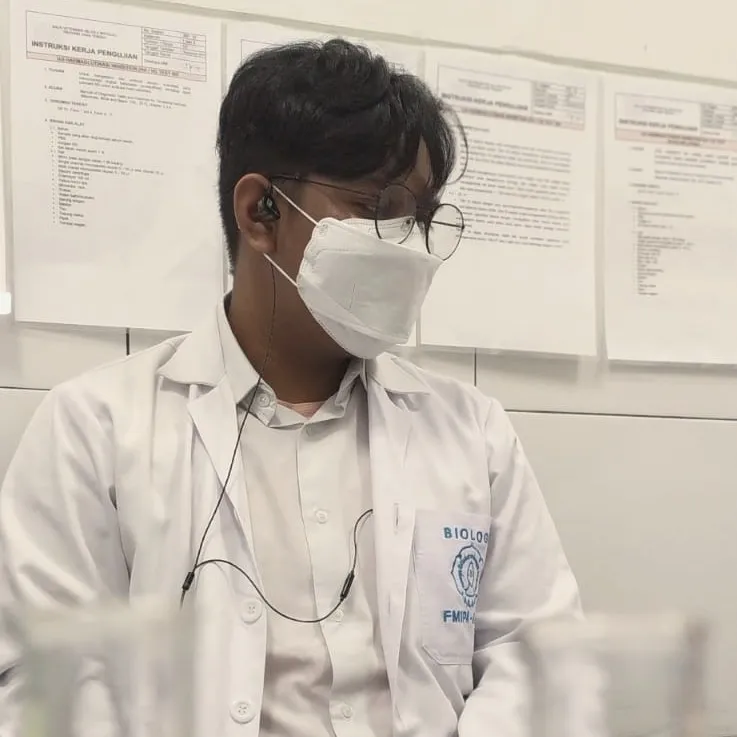 Engki Nandatama in a white lab coat at the bench, test tubes in the foreground